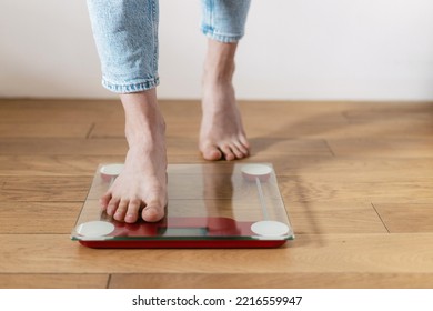 Cropped Shot Of Young Barefoot Woman In Casual Blue Jeans Step On The Floor Scales To Check Her Weight At Home. Concept Of Bmi Control And Keeping The Body In Shape