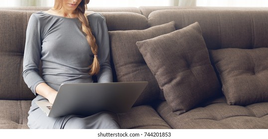 Cropped shot of young blond woman with braid working on a laptop sitting on the comfortable dark sofa at home, backlit warm light. Freelance or lifestyle concept. Empty space for your promotional text - Shutterstock ID 744201853