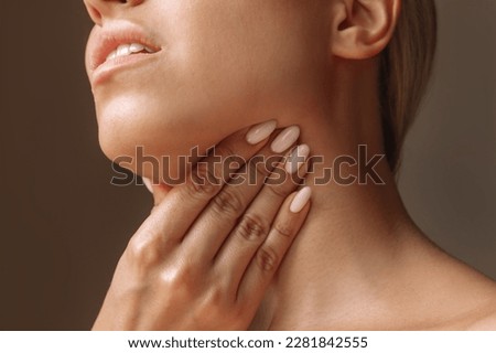Cropped shot of young blonde woman with throat ache touching enlarged lymph nodes under jaw on her neck on dark background. Flu, cold, covid, tonsillitis, sars virus, inflamed tonsils. Sore throat
