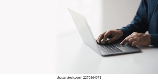 Cropped shot of young businessman hand typing on laptop computer while working in white modern office room.