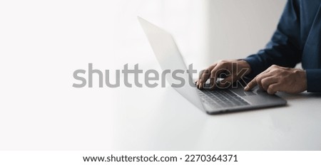Cropped shot of young businessman hand typing on laptop computer while working in white modern office room.