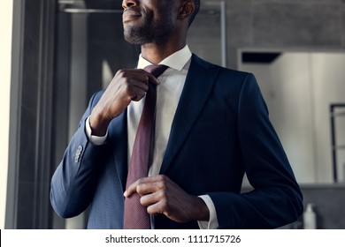 cropped shot of young businessman putting on his tie at bathroom