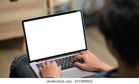 Cropped shot of young casual man using laptop computer while sitting on couch in living room.
