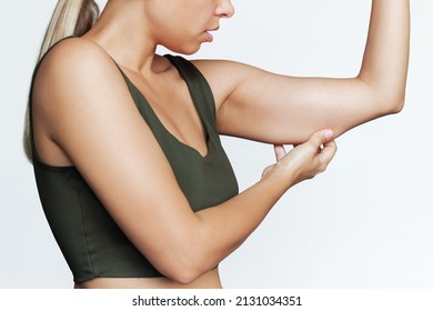 Cropped Shot Of A Young Caucasian Blonde Woman Grabbing Skin On Her Upper Arm With Excess Fat Isolated On A White Background. Pinching The Loose And Saggy Muscles. Overweight, Extra Weight Concept