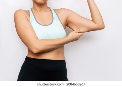 Cropped shot of young caucasian woman grabbing skin on her upper arm with excess fat isolated on a white background. Overweight, excess weight. Pinching the loose and saggy muscles.Taking care of body