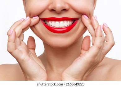 Cropped shot of young caucasian woman demonstrating the even teeth with her hands isolated on a white background. Perfect smile with red lipstick. Teeth whitening. Oral hygiene, dental health care