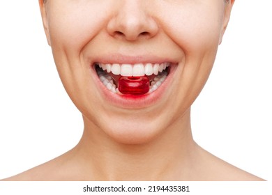 Cropped shot of a young caucasian woman keeping red lozenge for sore throat in her teeth isolated on a white background. Sucking candy in the mouth