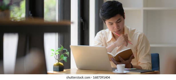 Cropped Shot Of Young College Student Concentrating On Book And Laptop To Prepare His Coming Exam 