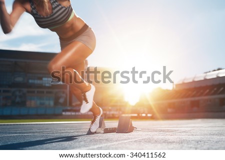 Cropped shot of young female athlete launching off the start line in a race. Female runner started the sprint from the starting line with bright sunlight.
