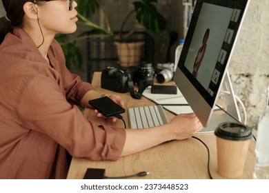 Cropped shot of young female photographer with smartphone sitting in front of computer screen and reviewing new images of fashion model - Powered by Shutterstock