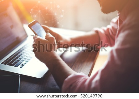 Cropped shot of a young man downloading in mobile store popular applications and multimedia programs. Man's hands using device at co-working office. Blurred background and infographics icons effect