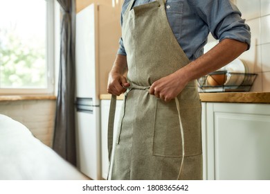 Cropped shot of young man, professional cook tying his apron while getting ready to prepare a meal, standing in the kitchen. Cooking at home concept. Selective focus. Horizontal shot - Powered by Shutterstock