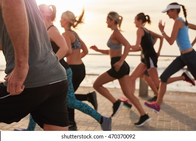 Cropped Shot Of Young People Running At Sunset. Group Of Men And Women Training Outdoors For Marathon Race.