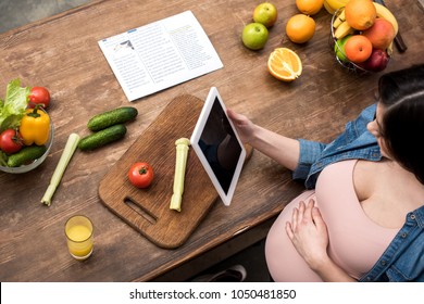 cropped shot of young pregnant woman holding digital tablet while cooking at kitchen - Powered by Shutterstock