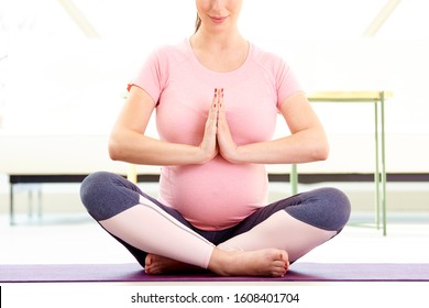 Cropped shot of young pregnant woman sitting in lotus pose and meditatiing on yoga mat.