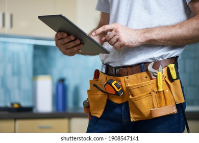 Cropped shot of young repairman wearing a tool belt with various tools using digital tablet while standing indoors - Powered by Shutterstock