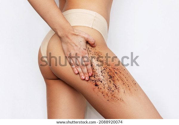 Cropped shot of young slender tanned woman massaging
her thigh with a anti-cellulite coffee scrub isolated on a white
background. Cosmetology, peeling, spa cosmetic products. Skin
care