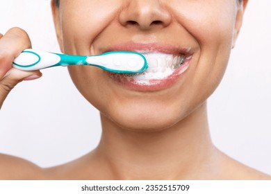 Cropped shot of a young smiling woman brushing her teeth with a toothbrush isolated on a white background. Morning and evening routine. Close up. High-quality teeth cleaning with foam formation - Powered by Shutterstock