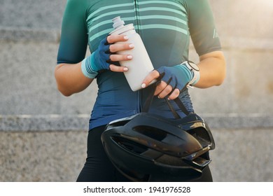Cropped shot of young sportswoman holding black bike helmet and water bottle while getting ready for cycling