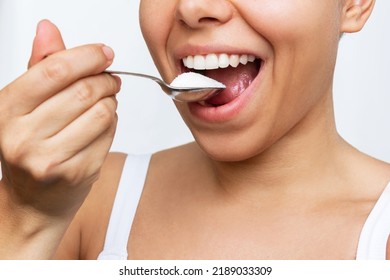 Cropped Shot Of A Young Woman Bringing A Spoonful Of Sugar To Her Mouth Isolated On A White Background. Sweet Tooth. Dependence, Harm And Danger To The Health Of White Sugar