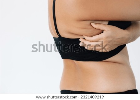 Cropped shot of a young woman grabbing skin with excess fat on her back under the arm above the bra isolated on a white background. Overweight, flabby and sagging muscles. Exercises for the back