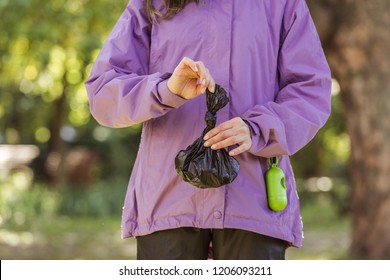 cropped shot of young woman holding trash bag while cleaning after pet in park