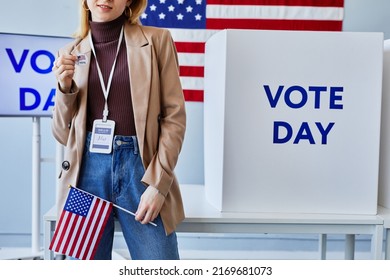 Cropped Shot Of Young Woman Holding I Vote Sticker While Standing In Voting Station With American Flag, Copy Space