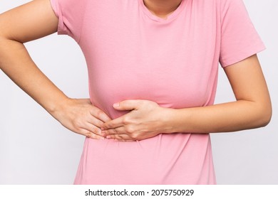 Cropped shot of a young woman in a pink t-shirt holding her side with her hands isolated on a white background. Sore side under the rib after training. Stomach pain