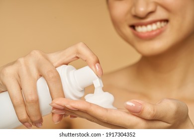 Cropped Shot Of Young Woman Smiling, Holding A Bottle Of Gentle Foam Facial Cleanser Isolated Over Beige Background