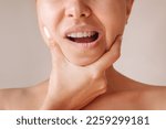Cropped shot of a young woman suffering from jaw pain holding her chin isolated on a beige background. Inflammation of cervical lymph nodes, Diseases of ENT organs, facial, trigeminal nerve, toothache