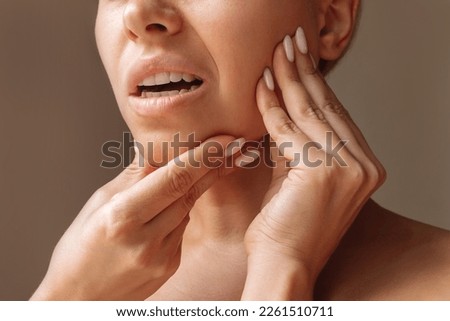 Cropped shot of young woman suffering from jaw pain holding her chin with hands on brown background. Inflammation of cervical lymph nodes, Diseases of ENT organs, facial, trigeminal nerve, toothache