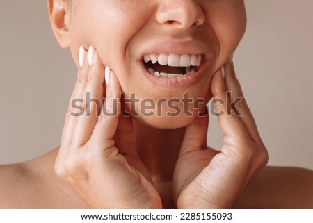 Cropped shot of a young woman suffering from jaw pain touching it with hands on a beige background. Inflammation of cervical lymph nodes, Diseases of ENT organs, facial, trigeminal nerve, toothache