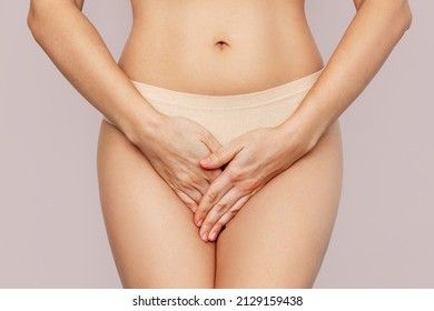 Cropped shot of a young woman in underwear holding her crotch with her hands, suffering from cystitis isolated on beige background. Gynecological problems, genital tract infections. Healthcare concept