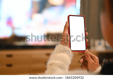 Cropped shot of young woman using blank screen mobile phone while sitting in living room.