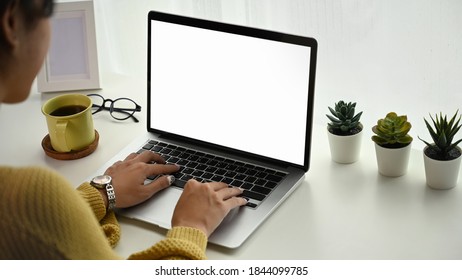 Cropped shot of young woman working with blank screen laptop on desk and workspace in living room.
