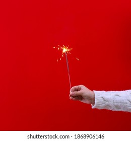 Cropped shot of young woman's hand in white knitted sweater holding the burning sparkler, isolated on red Christmas background. Close up, copy space for text. - Powered by Shutterstock