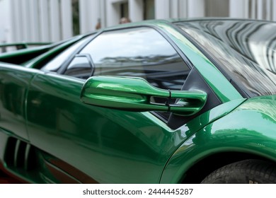 Cropped of side part of lamborghini coupe with rear view mirror and passenger door. Wing of collectible vehicle with shiny metallic covering outdoors