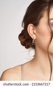 Cropped side portrait of a brown-haired lady in golden round stud earrings with a pendant made as an incandescent light bulb. The girl is posing on the gray background.