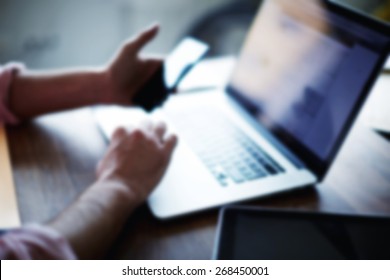 A cropped side shot of a young man working from home using smart phone and notebook computer, man's hands using smart phone in interior, man at his coworking place using technology blur effect