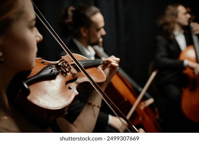 Cropped side view shot of unrecognizable female musician playing violin with chamber quartet on stage, focus on string instrument and bow