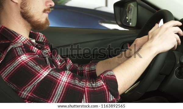 Cropped sliding shot of a bearded man sitting\
relaxed in a new car at the dealership with his hands on the\
steering wheel driving comfort safety insurance luxury lifestyle\
consumerism shopping\
buying.
