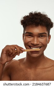 Cropped Of Smiling Black Guy Brushing His Teeth With Toothpaste. Young Brunette Curly Man With Naked Torso Looking At Camera. Dental Care And Hygiene. Isolated On White Background. Studio Shoot