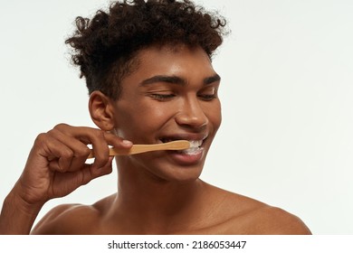 Cropped Of Smiling Black Guy Brushing His Teeth With Toothpaste. Young Brunette Curly Man With Naked Torso. Dental Care And Hygiene. Isolated On White Background. Studio Shoot. Copy Space