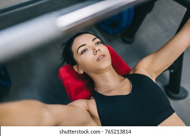 Cropped Top Shot Of Attractive Muscular Young Woman Workout In A Gym, Lying On A Bench, Lifting Weights With Barbell. People, Sport, Fitness Concpet.