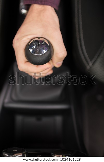 Cropped top\
view shot of a stylish young man holding gearshift while driving a\
car. Setting the speed\
acquired
