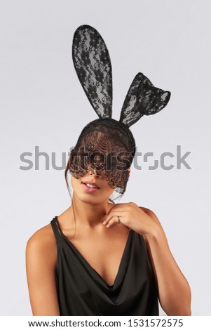 Cropped upper body's shot of a dark-haired girl, posing on a grey background. She is wearing black v-neck tank top and black headband with lace rabbit ears on her head and black lace veil. 