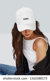 Cropped upward shot of a dark-haired girl, wearing white baseball cap with lettering 