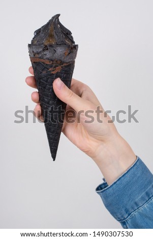 Cropped vertical close up view photo of hand in jeans denim shirt holding advertising showing tasty delicious icecream with brown sauce syrup isolated over grey background