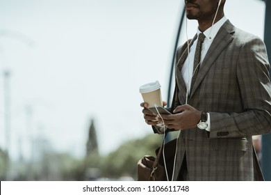 Cropped view of African american businessman wearing suit listening to music and holding coffee cup on train station - Powered by Shutterstock