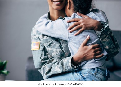 cropped view of african american daughter hugging mother in military uniform at home